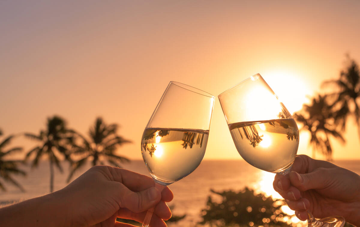 Cheers with wine glasses in a beautiful sunset beach setting.