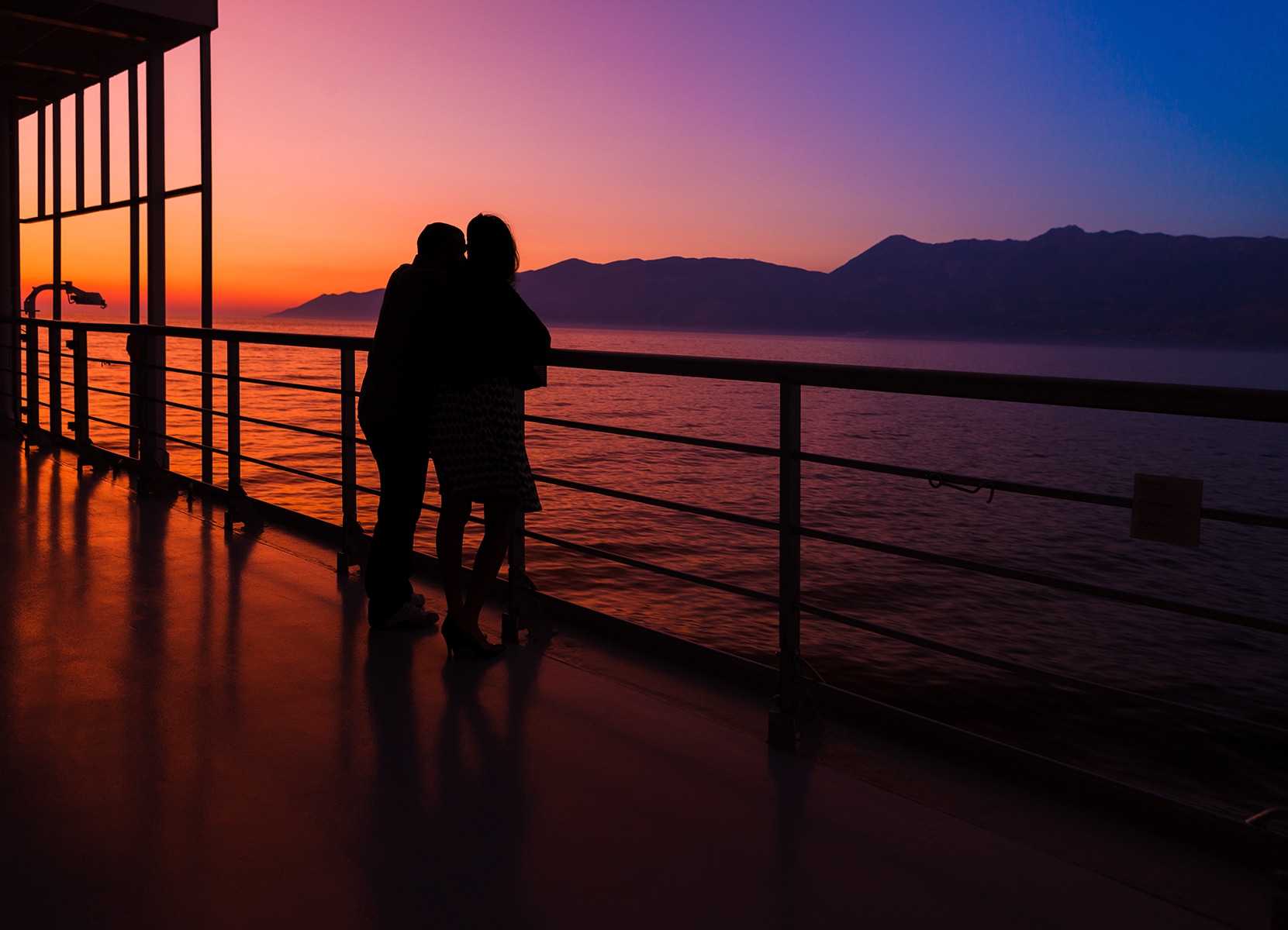 couple on silhouette by a cruise deck admiring the late sunset and the cost of corfu, greece